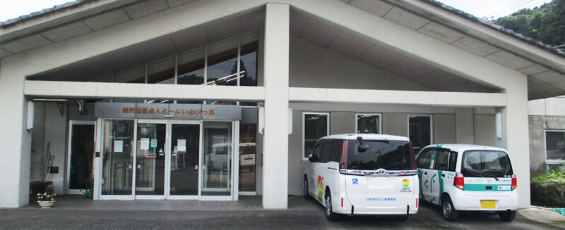 施設の玄関・車寄せ。白い建物に複数の送迎車が駐車されている